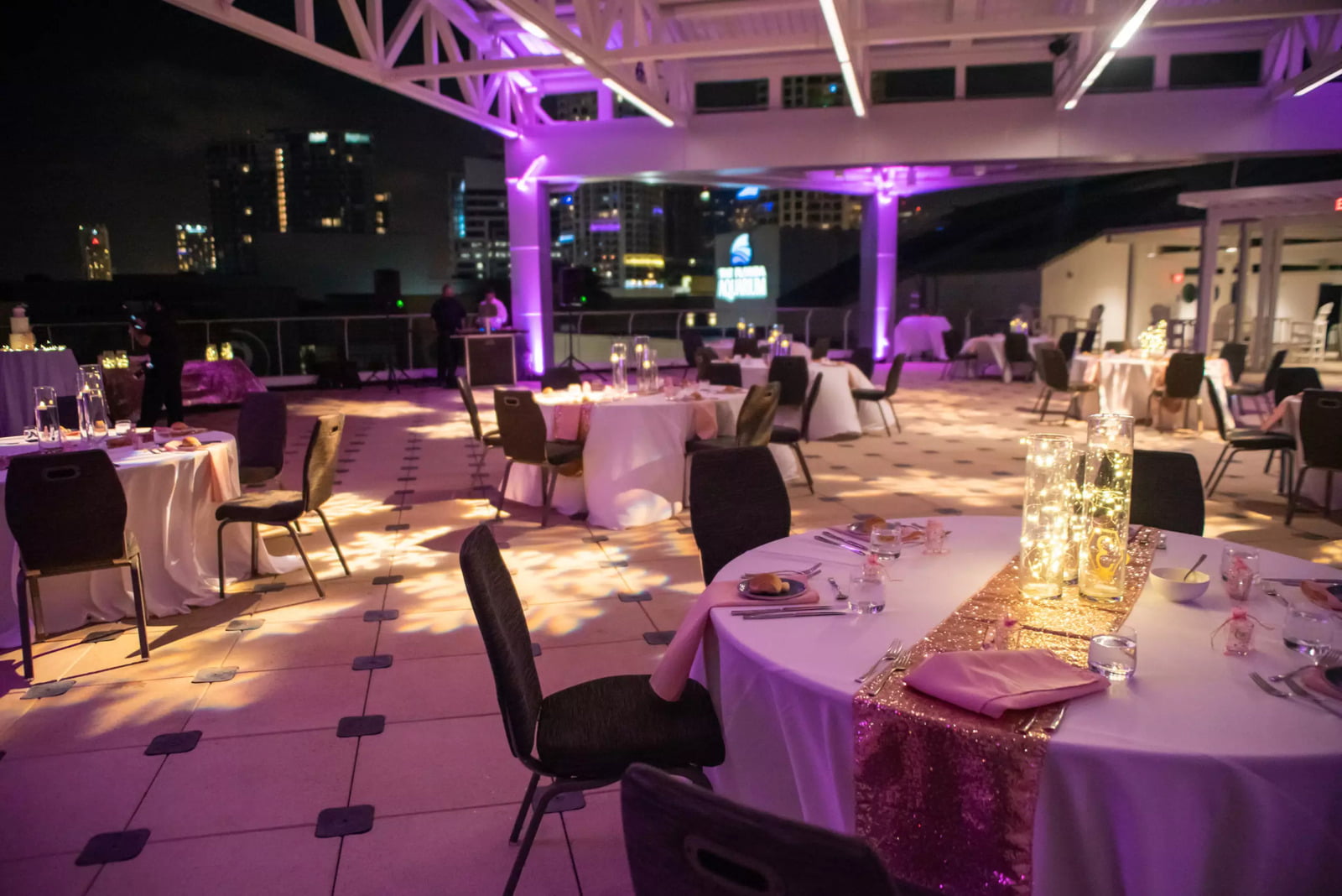 Rooftop terrace at the Florida Aquarium overlooking the downtown Tampa skyline. Round tables with chairs, decorative tablecloths and center pieces are spread out around the terrace. 
